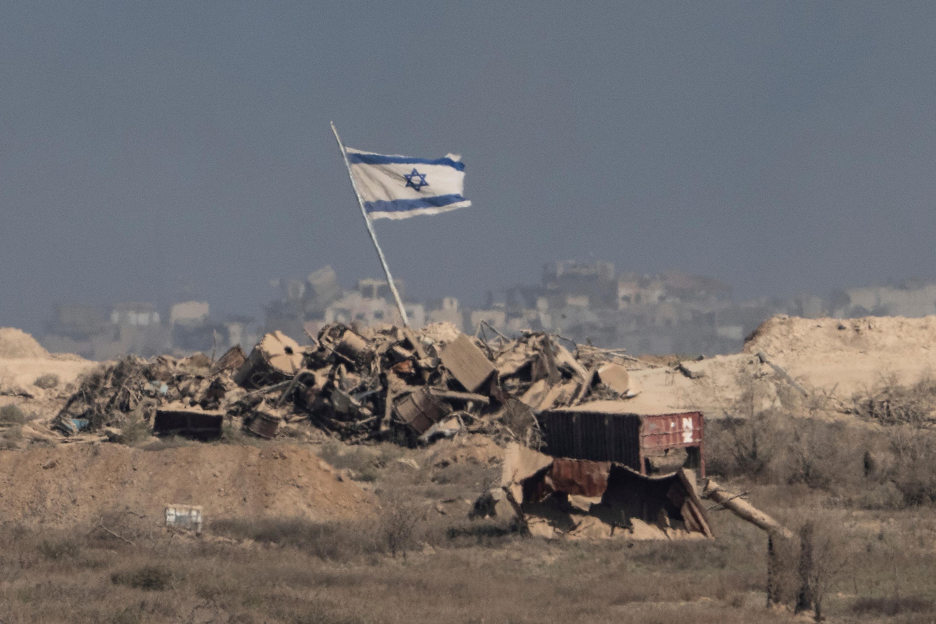 An Israeli flag waves over debris in an area of the Gaza Strip, as seen from southern Israel, Tuesday, Aug. 26, 2025. (AP Photo/Maya Levin/Courtesy)