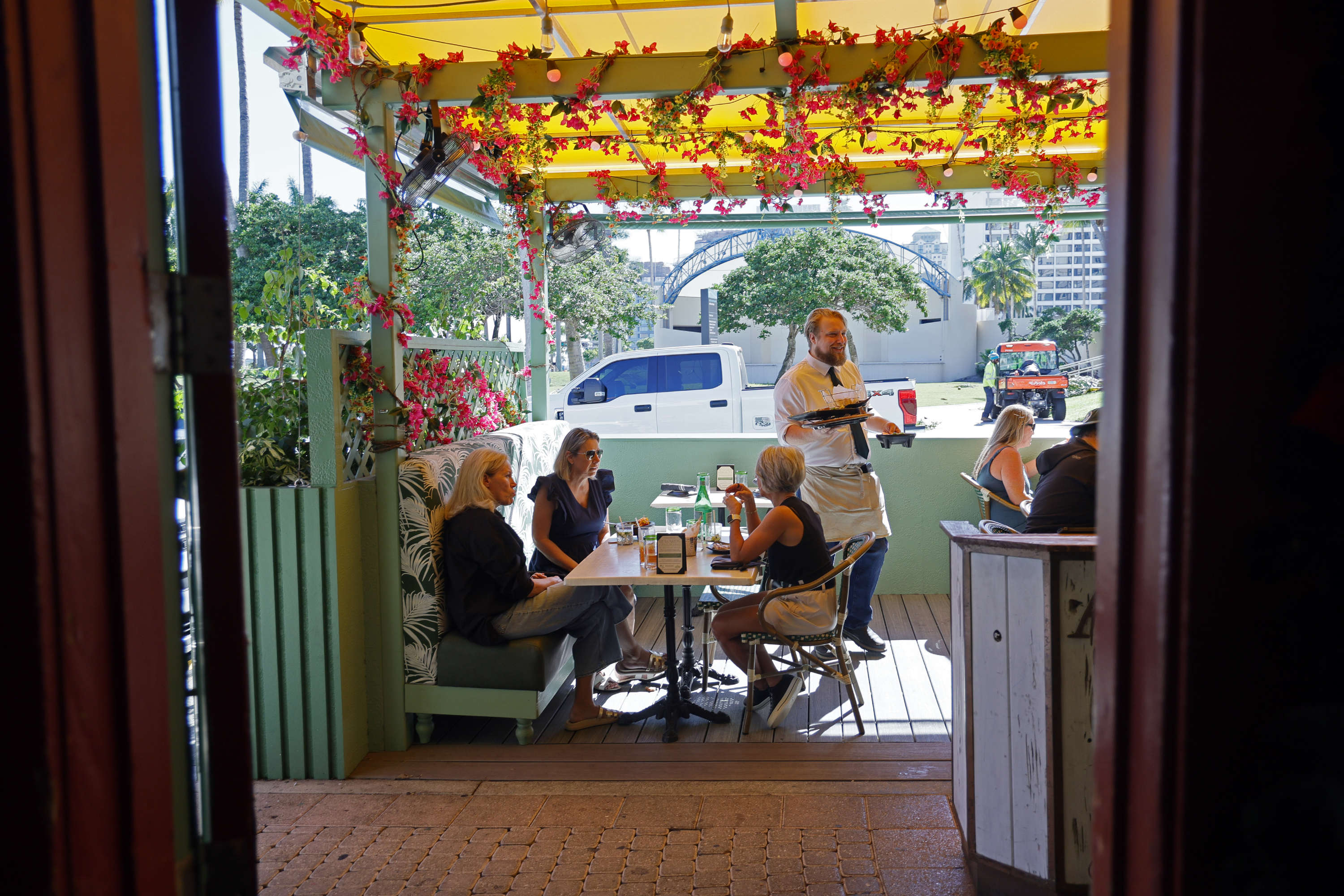 Server Noah Steiner clears dishes from a table in the “parklet” at Avocado Grill in West Palm Beach, on Thursday, Nov. 13, 2025. (Amy Beth Bennett / South Florida Sun Sentinel)